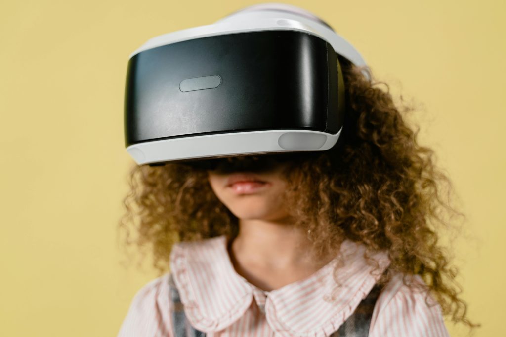 A person with curly hair wearing a virtual reality headset, appearing immersed in a digital experience, with a colorful background that suggests a tech-inspired environment.